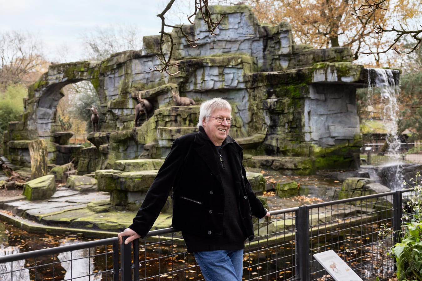 Man leunt lachend tegen hekje in Artis