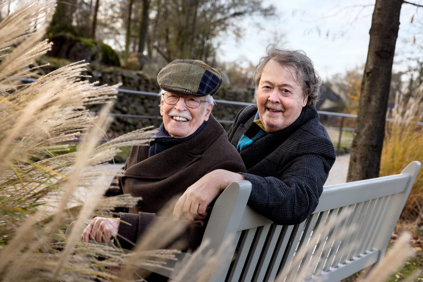 Twee mannen zittend op bankje in Artis, kijken lachend in camera