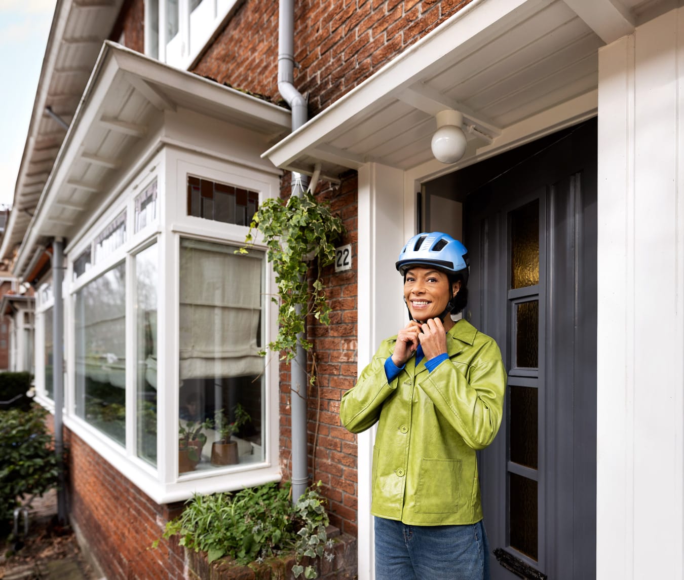 Lachende vrouw met groene jas zet fietshelm op voor haar huis voor veiligheid campagne Vervoerregio Amsterdam