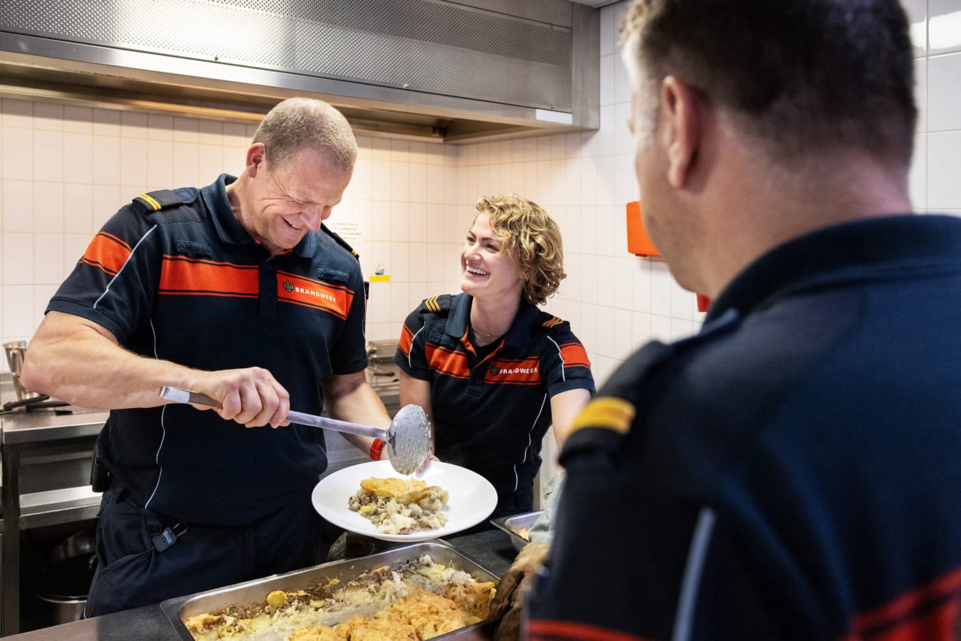 Brandweerman en vrouw lachen tijdens het opscheppen van eten in de keuken