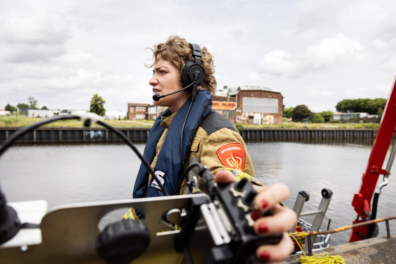 Brandweervrouw spreekt aan het water met duiker via headset, rode nagels
