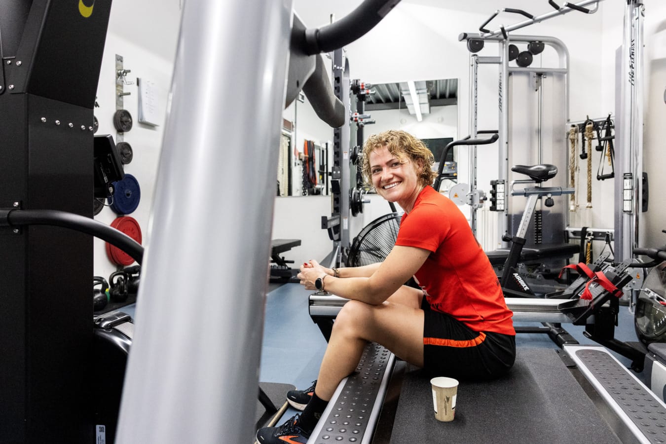 Brandweervrouw lacht in camera, zittend op loopband in fitness ruimte