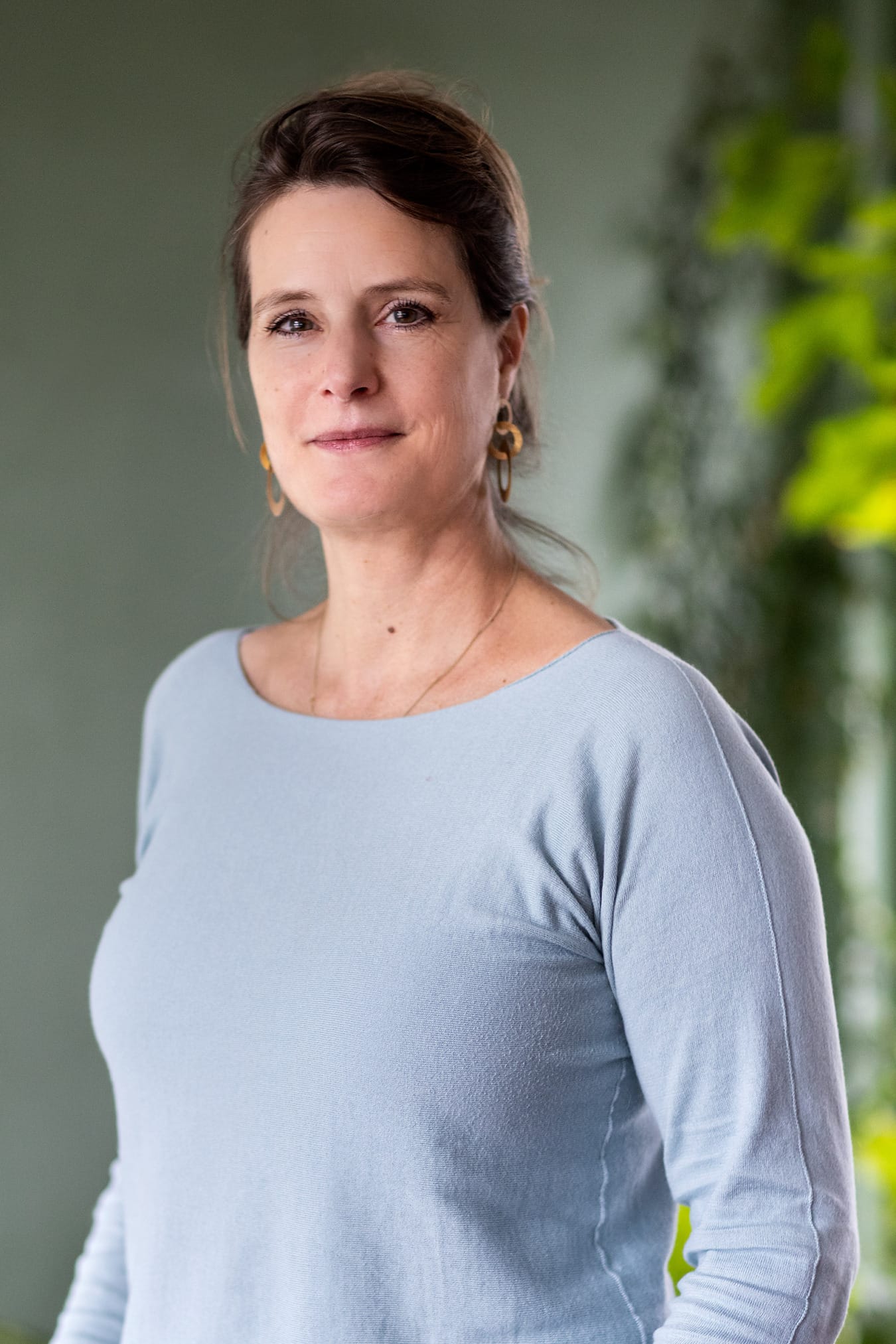 Vrouw in blauw kijkt glimlachend in camera in groene ruimte met planten